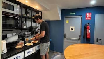 A kitchen area with a person preparing food, a waste bin, and a fire extinguisher.