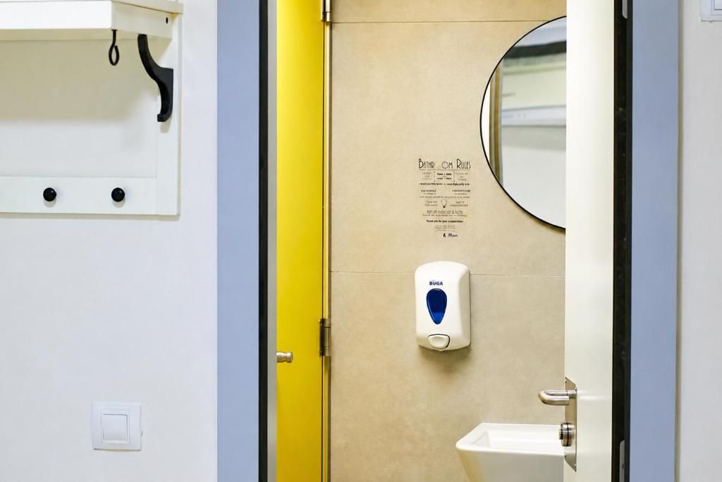 Un baño con dispensador de gel antibacterial, un espejo y un cartel con indicaciones.