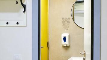 Un baño con dispensador de gel antibacterial, un espejo y un cartel con indicaciones.