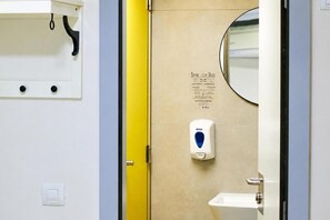 Toilet med håndspritdispenser, spejl og et skilt med regler.