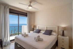 Ein Hotelzimmer mit einem Bett, einem Nachttisch, einer Lampe, einem Deckenventilator und Blick aufs Meer.