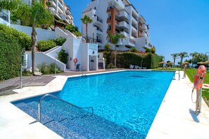 Ein Swimmingpool mit klarem, blauem Wasser, umgeben von einem weißen Gebäude mit Balkonen und einem Garten.