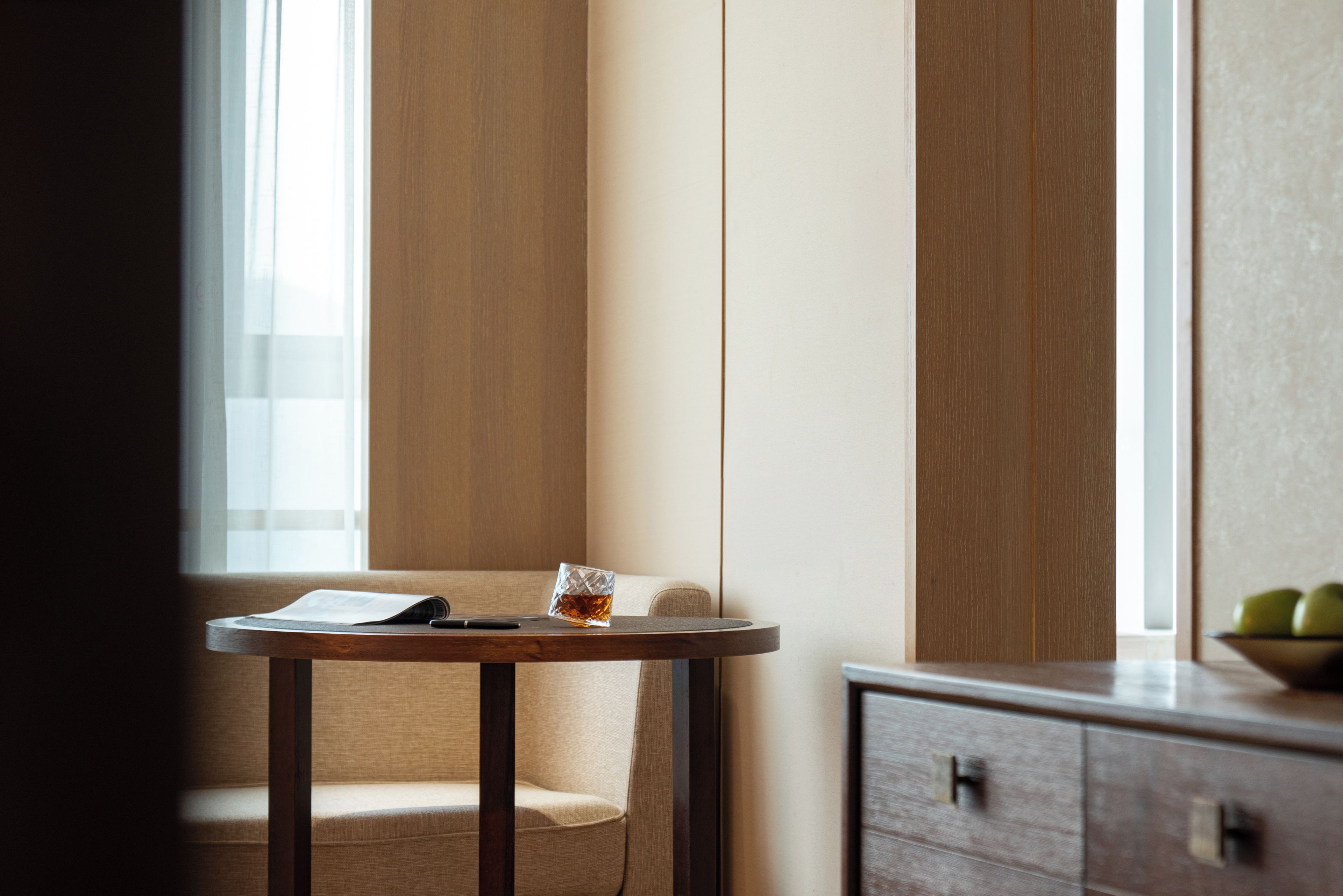 A corner of a room with a wooden chair, a small round table, and a glass of amber liquid.