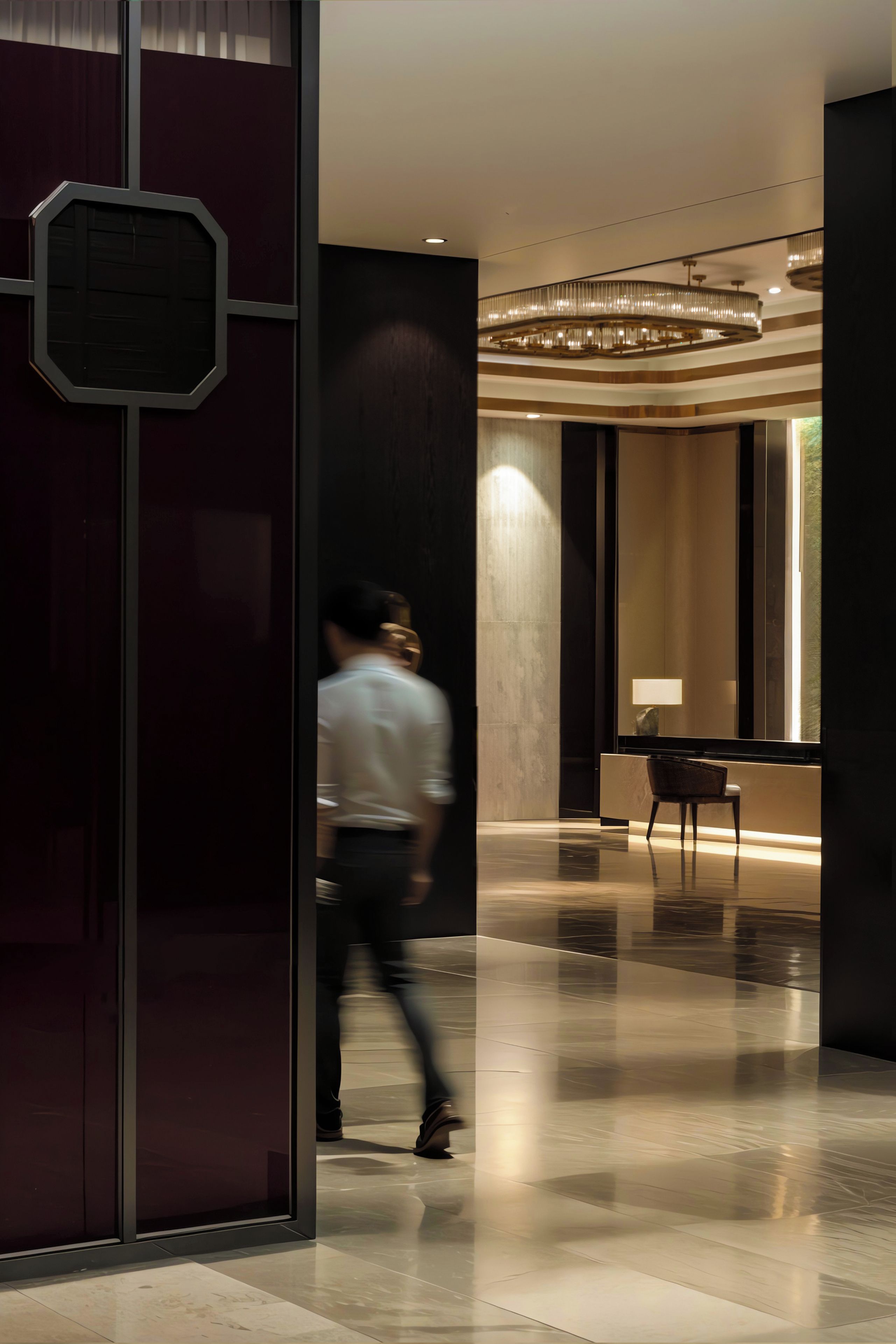 A modern interior with a reflective floor, a glass partition, and a seating area with a lamp.