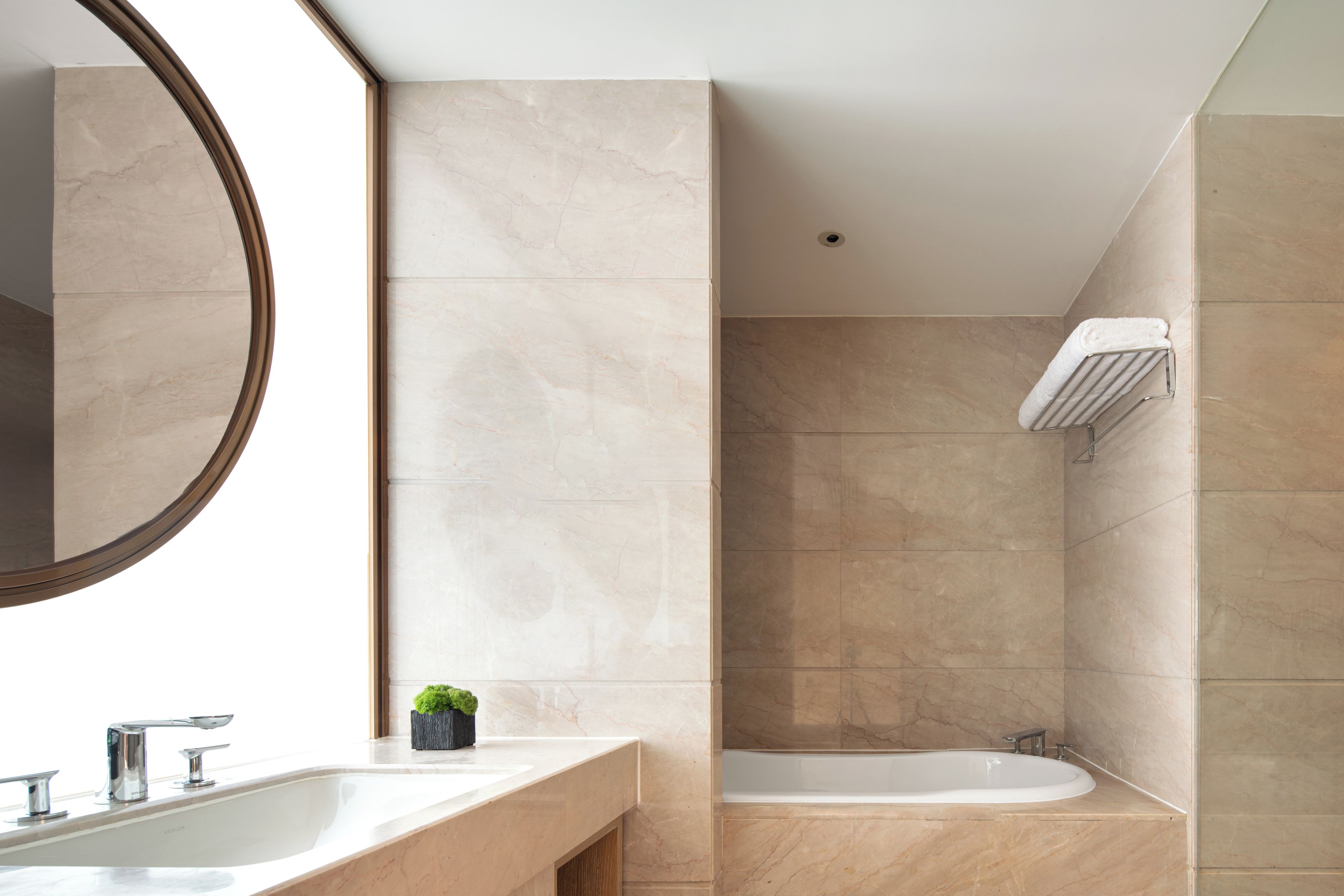 A bathroom with a large mirror, a sink, a small plant, and a bathtub.