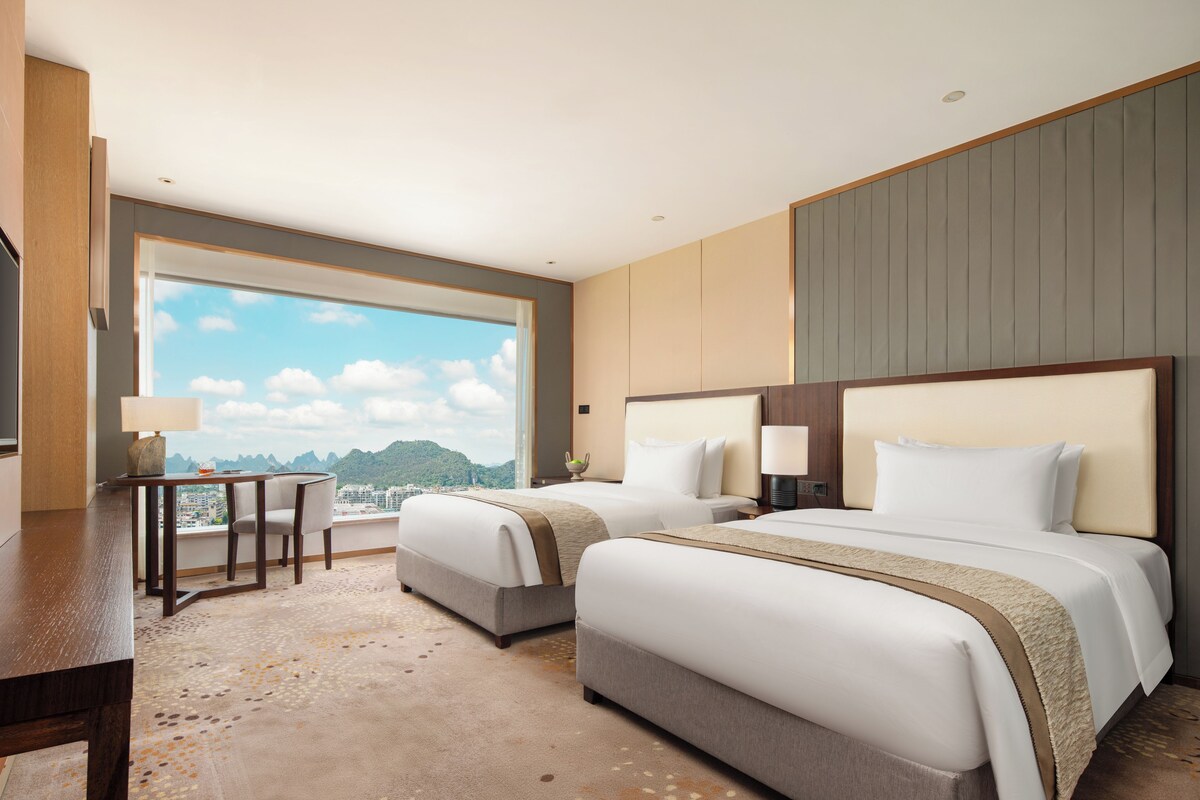 A hotel room with two beds, a desk, and a view of the mountains.