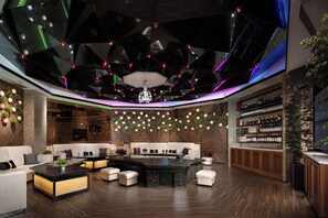Un área de lounge moderna con un mobiliario central, un bar y una pared de estanterías llenas de botellas.