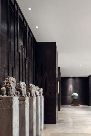 Un interior moderno con una pared de madera oscura, una serie de estatuas de leones de piedra y un objeto esférico sobre un pedestal.