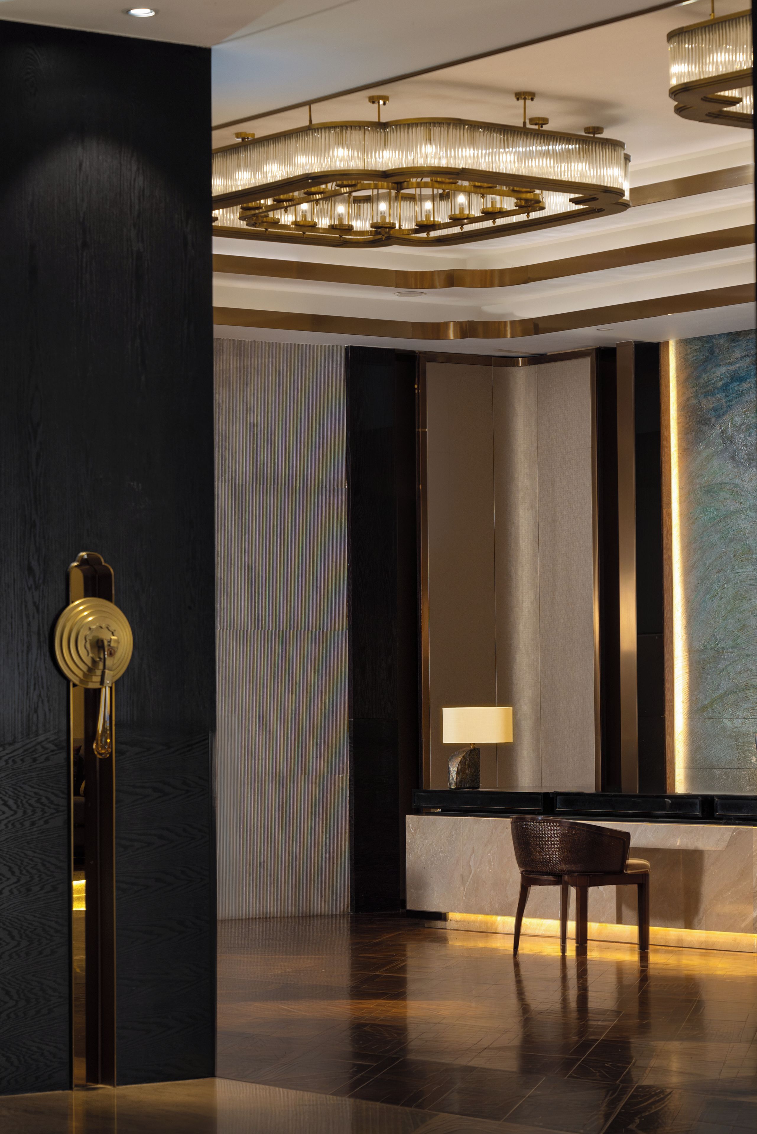 Un hall d’entrée moderne agrémenté d’un lustre, d’un miroir, d’une lampe et d’un fauteuil.
