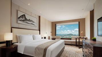 A hotel room with a large bed, a desk, a chair, a TV, and a window with a city view.
