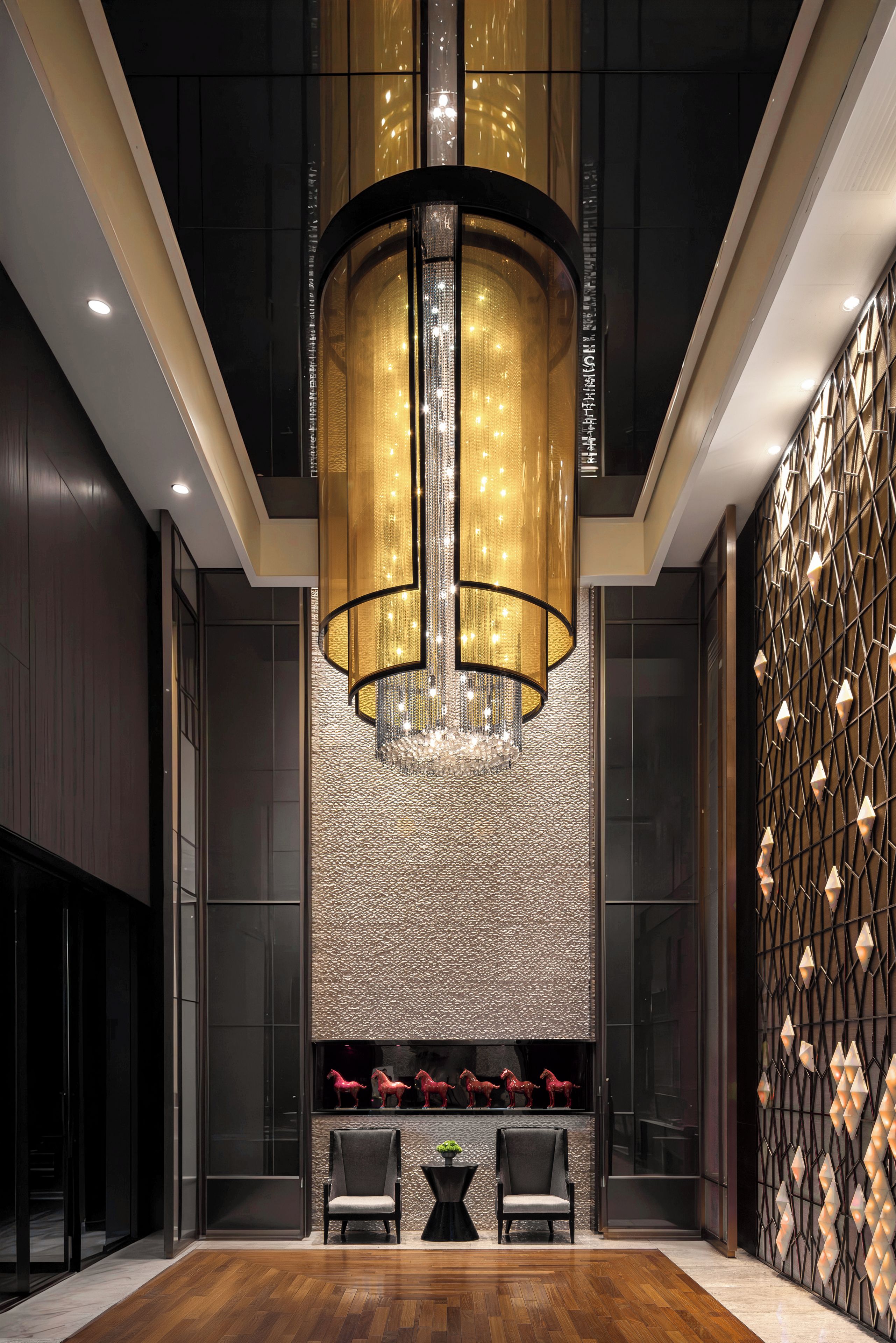 A modern lobby with a large chandelier, seating area, and decorative wall panels.