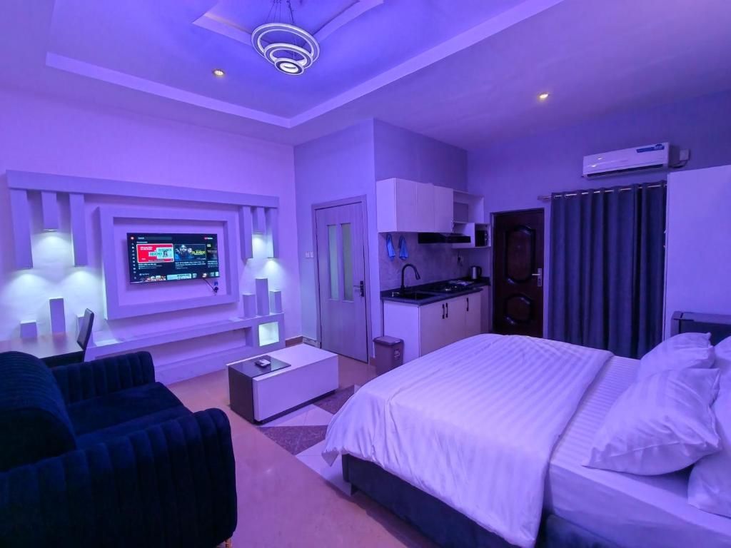 Ett modernt hotellrum med en säng, en TV som är monterad på väggen, ett litet kök och en sittgrupp med en soffa.