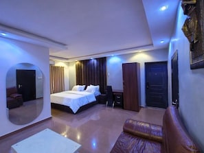 A modern hotel room with a large bed, a seating area, a desk, and a mirror. - Milestone Boutique Apartments (ikeja)