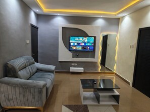 Una sala de estar moderna con un sofá gris, un televisor de pantalla plana montado en la pared y una mesa de centro de vidrio.