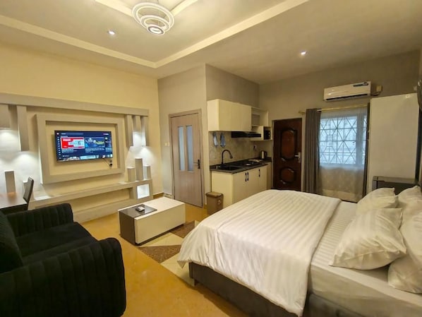 Habitación de hotel con cama, televisión montada en la pared, kitchenette y ventana con cortinas.
