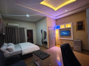 Quarto de hotel com cama, mesa de cabeceira, televisão e espelho.