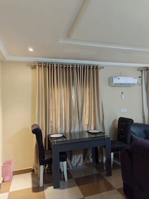 A dining area with a table, chairs, and an air conditioning unit mounted on the wall. - Milestone Boutique Apartments (ikeja)