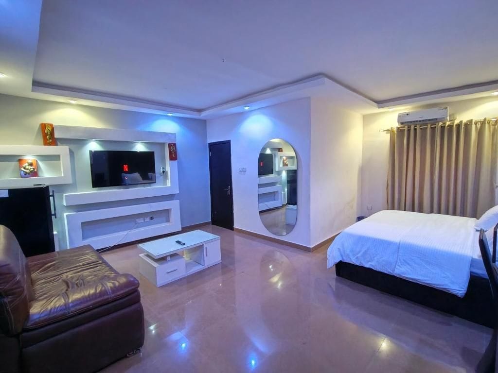 Habitación de hotel moderna con televisor de pantalla plana, cama, zona de estar y espejo.