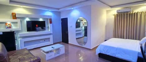 A modern hotel room with a flat-screen TV, a bed, a seating area, and a mirror.