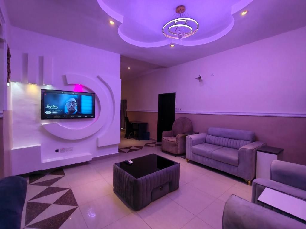 A modern living room with a flat-screen TV mounted on the wall, a black ottoman, and a purple sofa.