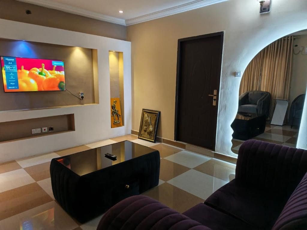A modern living room with a flat-screen TV mounted on the wall, a black coffee table, and a purple sofa.