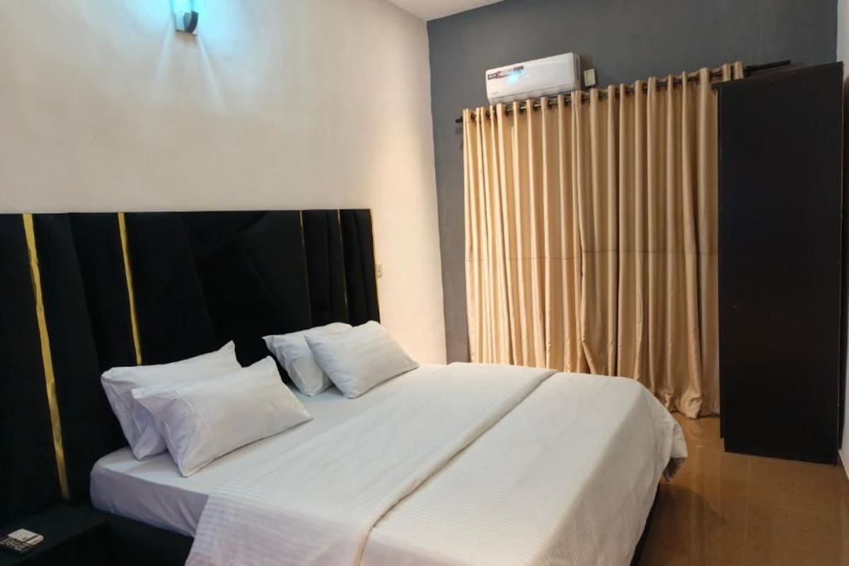 A hotel room with a bed, a nightstand, a wall-mounted air conditioning unit, and a curtain.