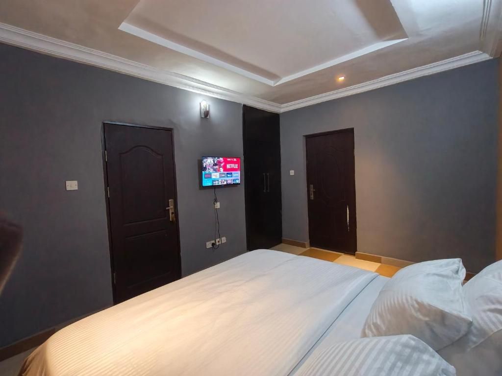 Quarto de hotel com uma cama, duas portas, televisão de tela plana na parede e teto com iluminação embutida.
