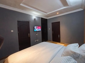 A hotel room with a bed, two doors, a flat-screen TV mounted on the wall, and a ceiling with recessed lighting. - Milestone Boutique Apartments (ikeja)