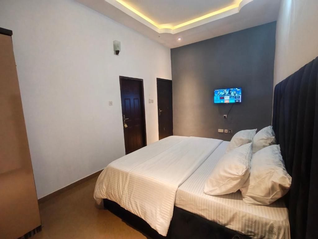Un dormitorio con cama, televisión instalada en la pared y una puerta.
