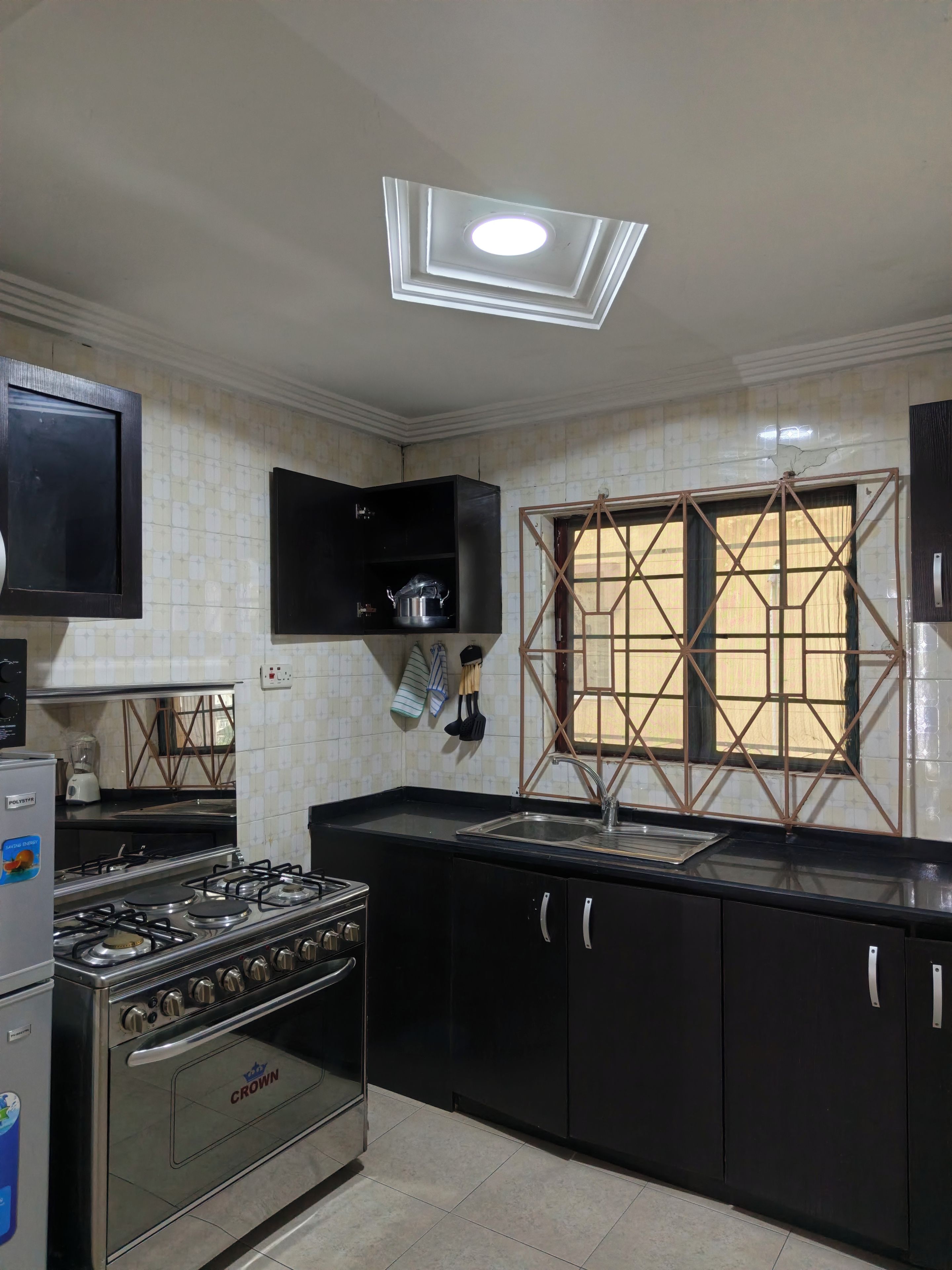 Una cocina con estufa a gas, horno, gabinetes negros, un lavamanos y una ventana con un diseño geométrico.