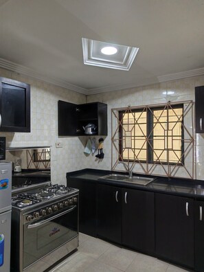 Una cocina con estufa a gas, horno, gabinetes negros, un lavamanos y una ventana con un diseño geométrico.