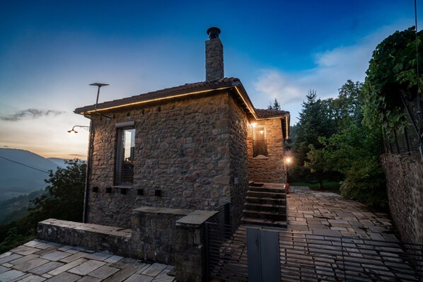 A stone building with a chimney, a small window, and a staircase leading to a door.