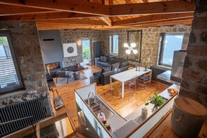 A modern interior with a stone wall, wooden beams, a sofa, a dining table, and a kitchen area.