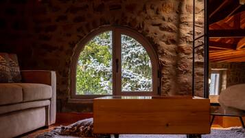 A cozy room with a stone wall, a large arched window, a wooden bench, and a sofa.