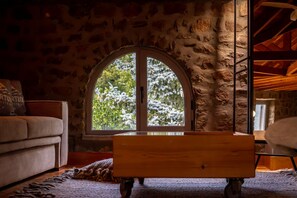 A cozy room with a stone wall, a large arched window, a wooden bench, and a sofa.
