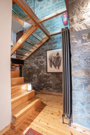 Una escalera de madera conduce a una zona superior con una pared de piedra y un cuadro enmarcado de un bisonte.