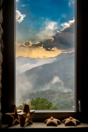A window with a view of a mountainous landscape, a star-shaped object, and a candle on a windowsill.