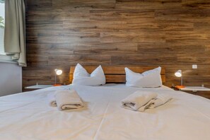 A neatly made bed with white linens and pillows, two bedside lamps, and a wooden headboard. - Residence Margarete 1.13 (Ostseebad Binz)