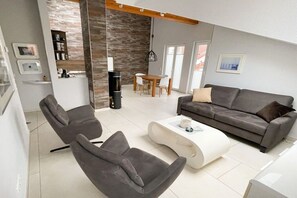 A modern living room with a grey sofa, two armchairs, a coffee table, and a dining area with a wooden table and chairs. - Residence Margarete 1.13 (Ostseebad Binz)