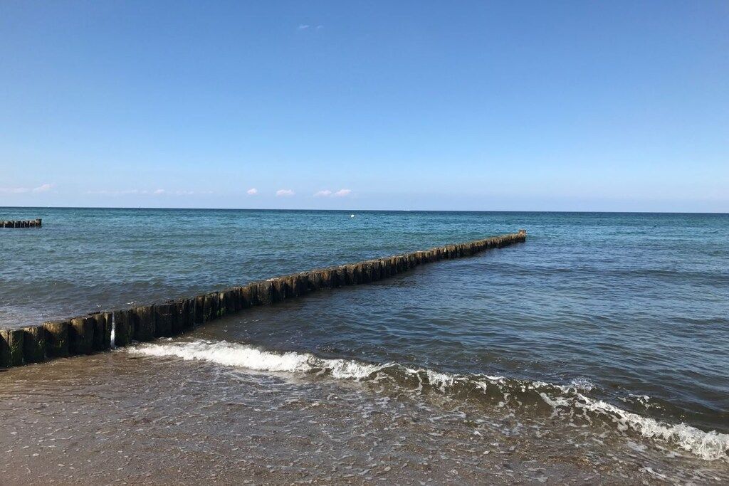 Une plage avec une jetée en bois qui s’avance dans l’eau, un ciel dégagé et une mer calme.