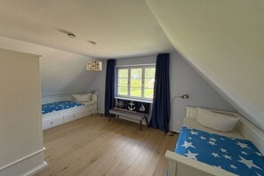 A bedroom with a sloped ceiling, a window with curtains, a bed with a star-patterned bedspread, a bench with nautical decorations, and a bedside table. - Zanzibar under a thatched roof (Ostseebad Rerik)