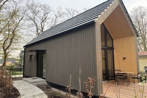 A modern building with a sloped roof, a wooden deck, and a small outdoor seating area. - Lodges Usedom - Holiday Home 3 (Koserow)