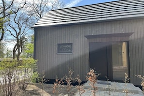 A modern building with a dark exterior, a large glass door, and a small window. - Lodges Usedom - Holiday Home 3 (Koserow)