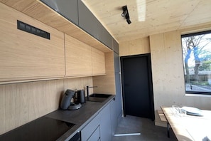 A modern kitchen with wooden cabinetry, a black countertop, and a window providing natural light. - Lodges Usedom - Holiday Home 3 (Koserow)