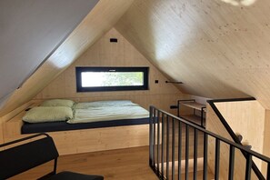 Ein kleiner Raum mit schrägem Dach, einem Bett, einem Fenster und einer Treppe.
