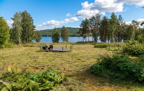 A lakeside outdoor seating area with a deck, surrounded by trees and vegetation.