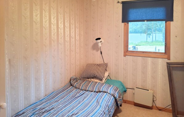 A small room with a single bed, a radiator, a window with a view of the outdoors, and a wall-mounted lamp.