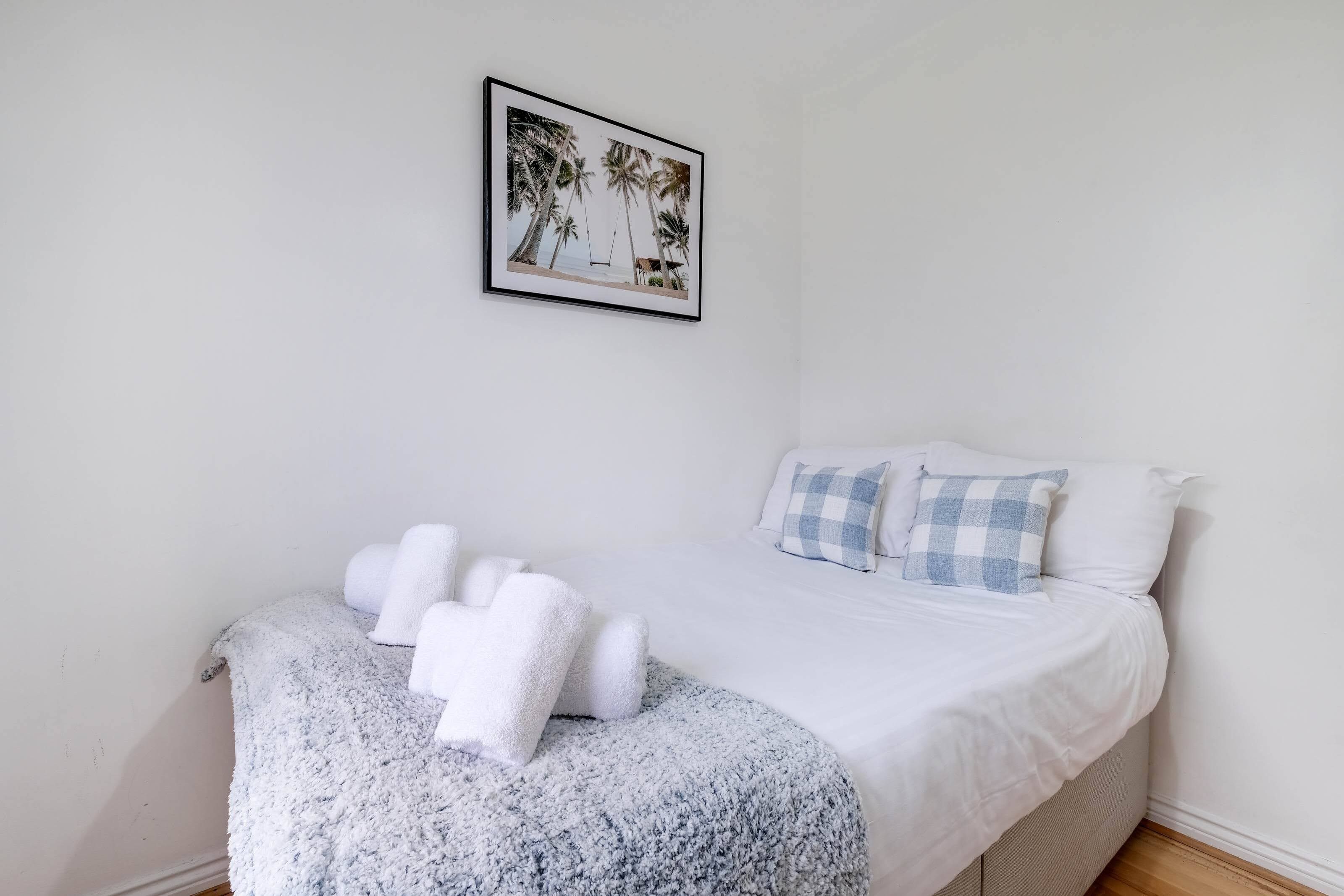 Een slaapkamer met een bed, kussens, een dekbed en een lijst met een foto aan de muur.