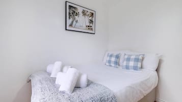 Een slaapkamer met een bed, kussens, een dekbed en een lijst met een foto aan de muur.