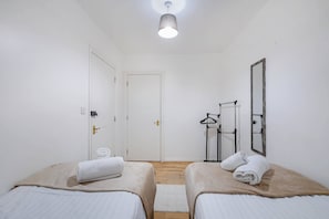 Et værelse med to senge, en dør, et spejl og en loftlampe.